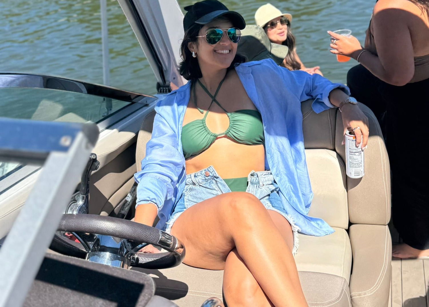 Woman in a bikini and blue jacket sitting on a boat with a scenic water background